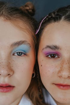 Two women with distinct colorful eye makeup and freckles captured in a close-up studio portrait.
