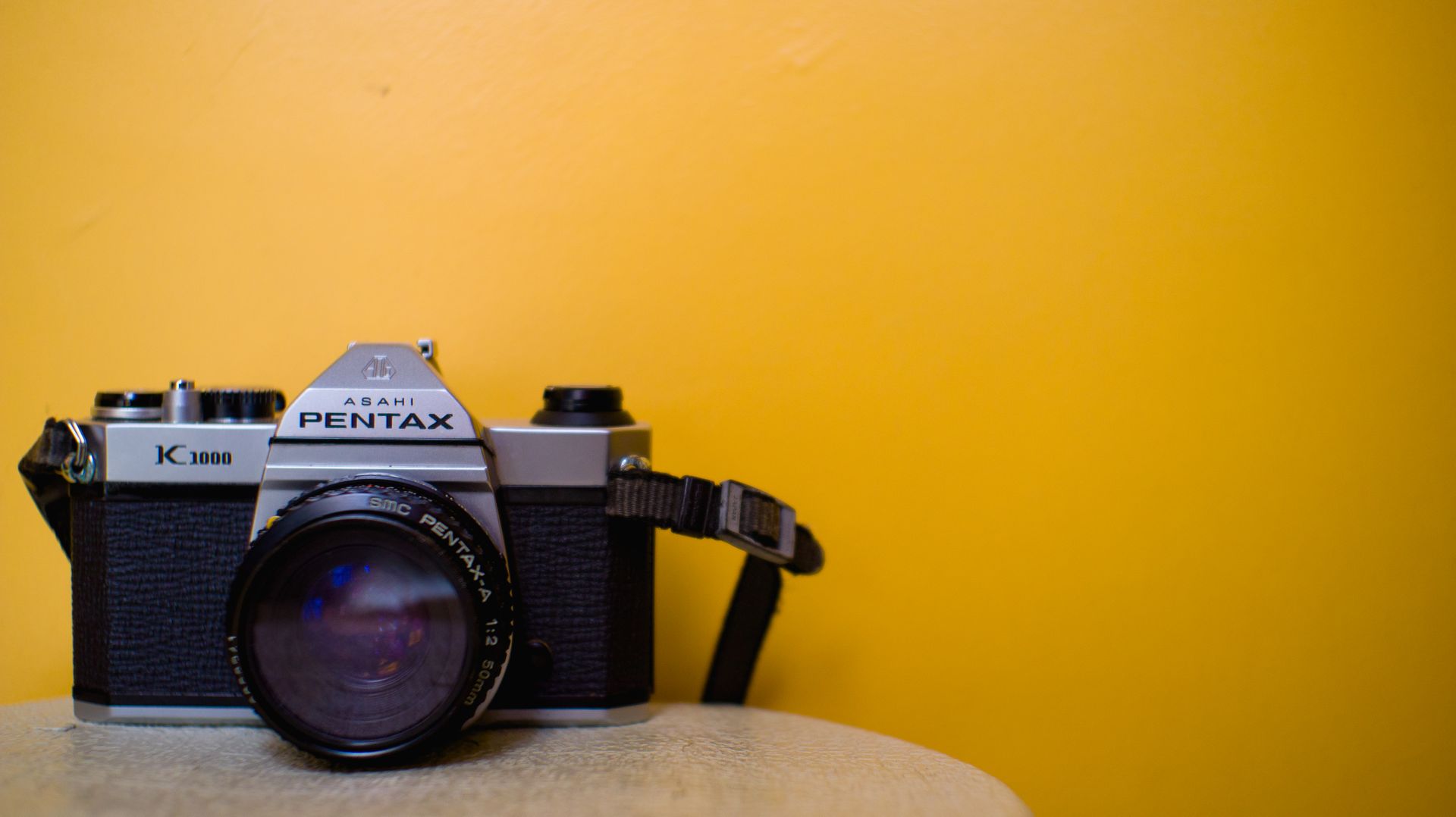 Vintage film camera with lens on a bright yellow background, perfect for product photography and design projects.