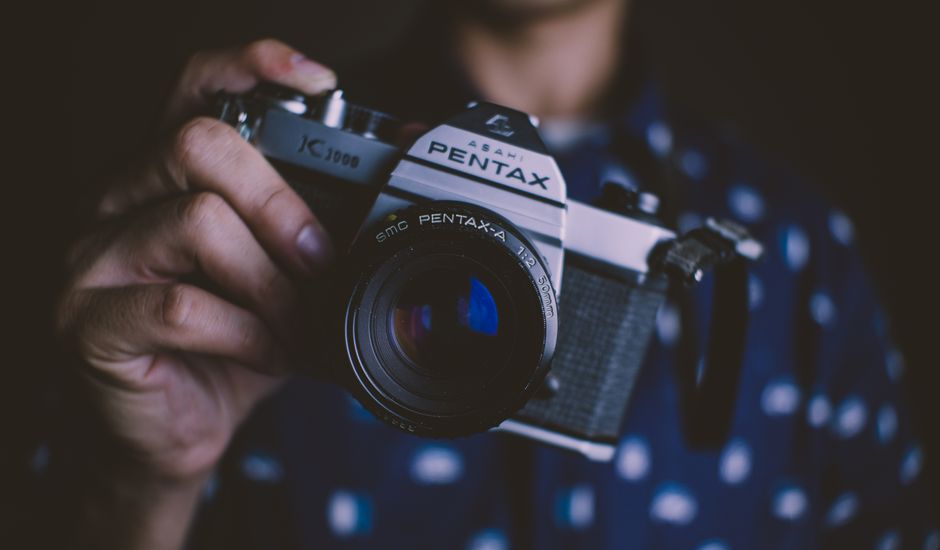 Fotógrafo segurando câmera SLR analógica 35mm na altura dos olhos em rua urbana com fundo desfocado