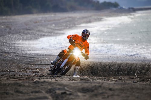 Free A Man in Orange Jacket and Black Helmet Riding a Motorcycle Stock Photo