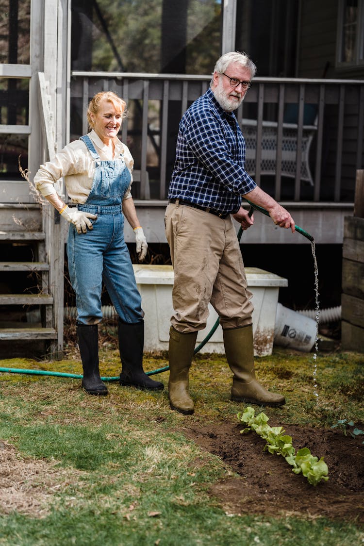 Senior Couple Watering Plants In Garden