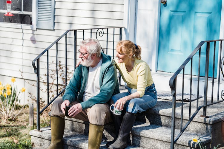 Husband And Wife Sitting On Porch With Cups Of Tea