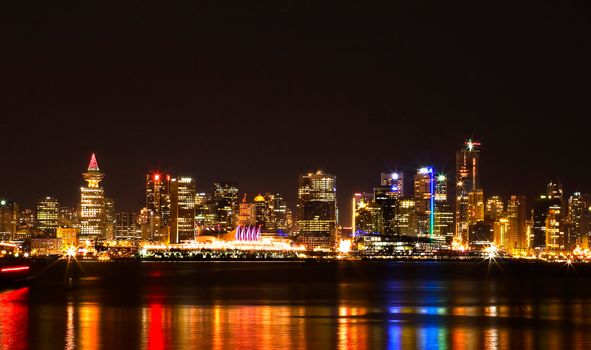 A stunning night view of Vancouver's illuminated skyline reflecting on the water.