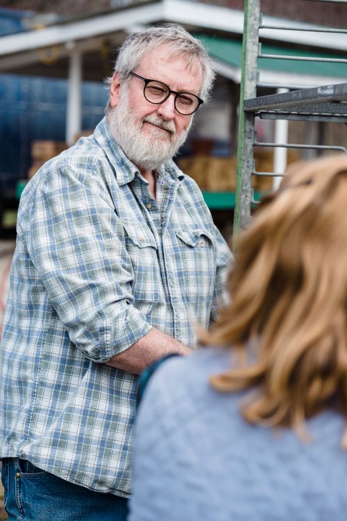 Free Positive senior male farmer in checkered shirt with gray hair standing near metal shelves on backyard and looking at camera in sunlight Stock Photo