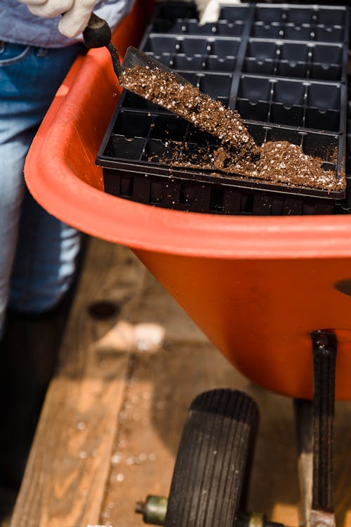 Free From above of crop unrecognizable gardener pouring soil into black plastic box in greenhouse Stock Photo