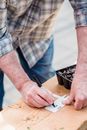 Crop unrecognizable male wearing jeans and shirt holding pen and writing on paper lying on wooden board