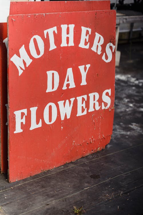 Red battered signboard with painted surface with phrase mothers day flowers placed on dark wooden floor