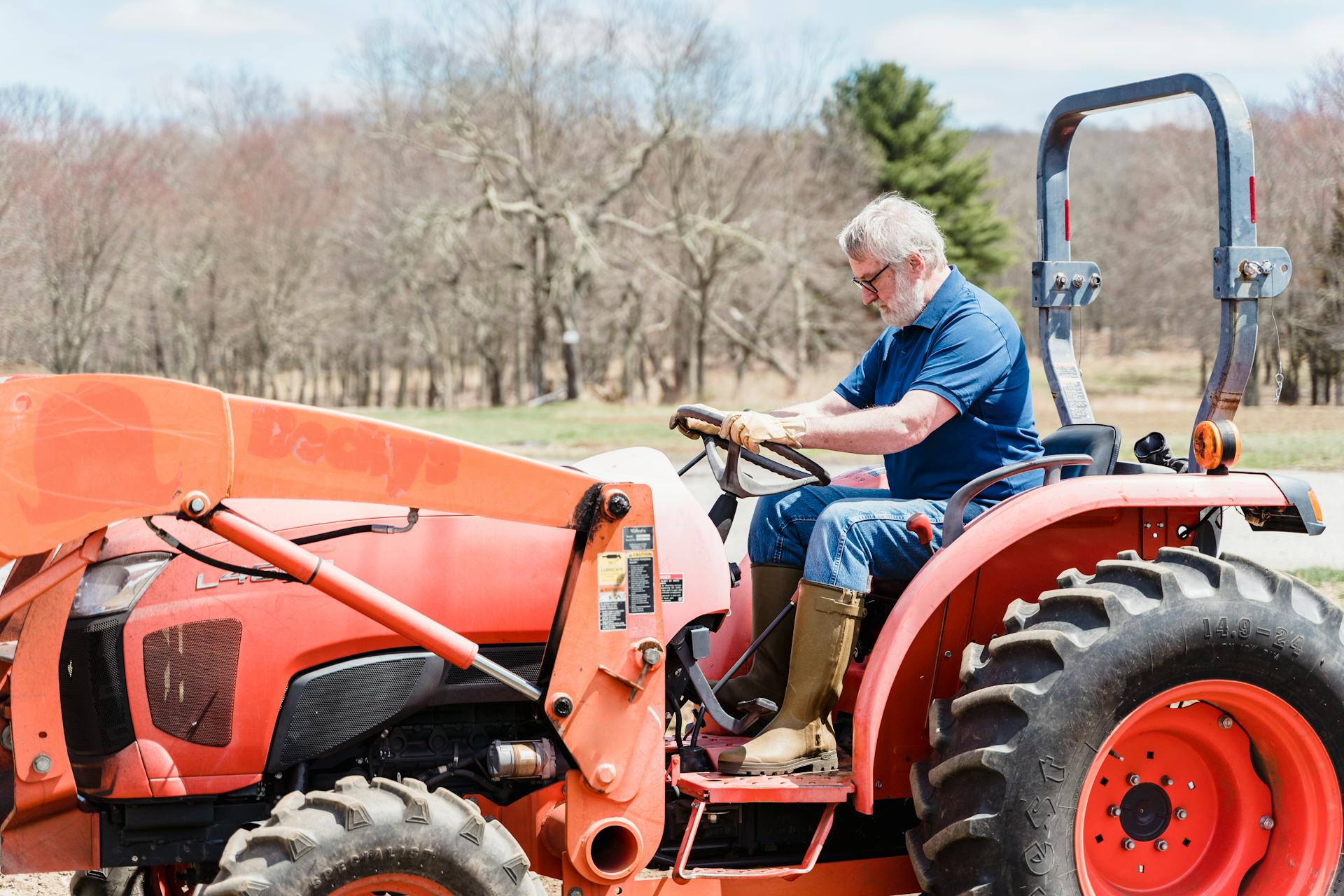 Elderly man driving a tractor on a sunny day in a rural setting, symbolizing agriculture and farming life.