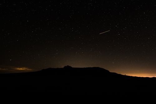 Free A breathtaking starry night sky featuring a shooting star over a mountain silhouette. Stock Photo
