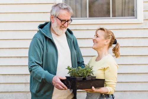 Free Happy elderly couple enjoying gardening, sharing moments while holding potted plants. Stock Photo