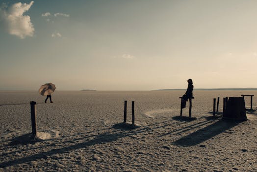 A person walks with an umbrella in a vast Turkish salt desert during sunset, creating striking shadows.