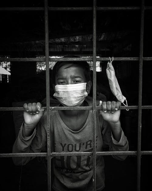 Free A Boy Wearing a Face Mask Behind the Metal Fence Stock Photo