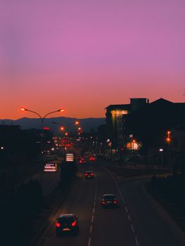 A scenic city road under a twilight sky with cars and illuminated buildings, capturing urban nightlife.