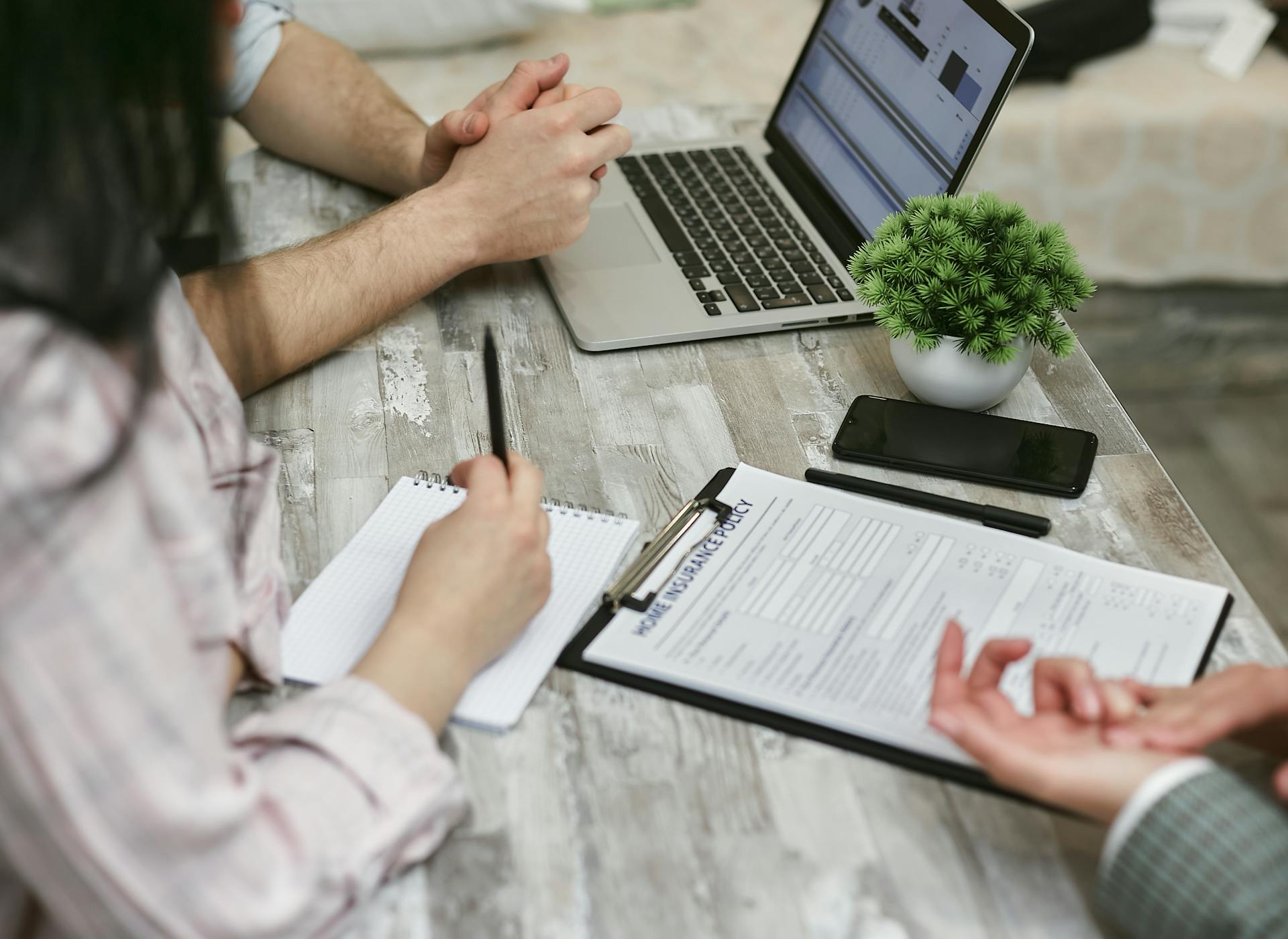 Professionals discussing home insurance policy over laptop and notes in an office setting.