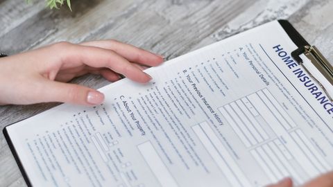 Close-up of hands holding a home insurance document indoors, showing personal details section.