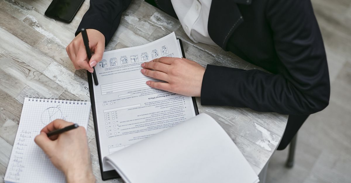 Two colleagues reviewing documents and taking notes during a business meeting.