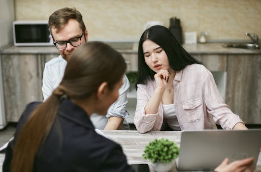 Three coworkers engaged in a discussion around a laptop in a modern office setting.