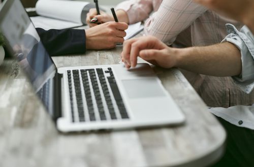 Free Crop faceless colleagues sitting at table while working on laptop and taking notes on documents with pen in light office Stock Photo