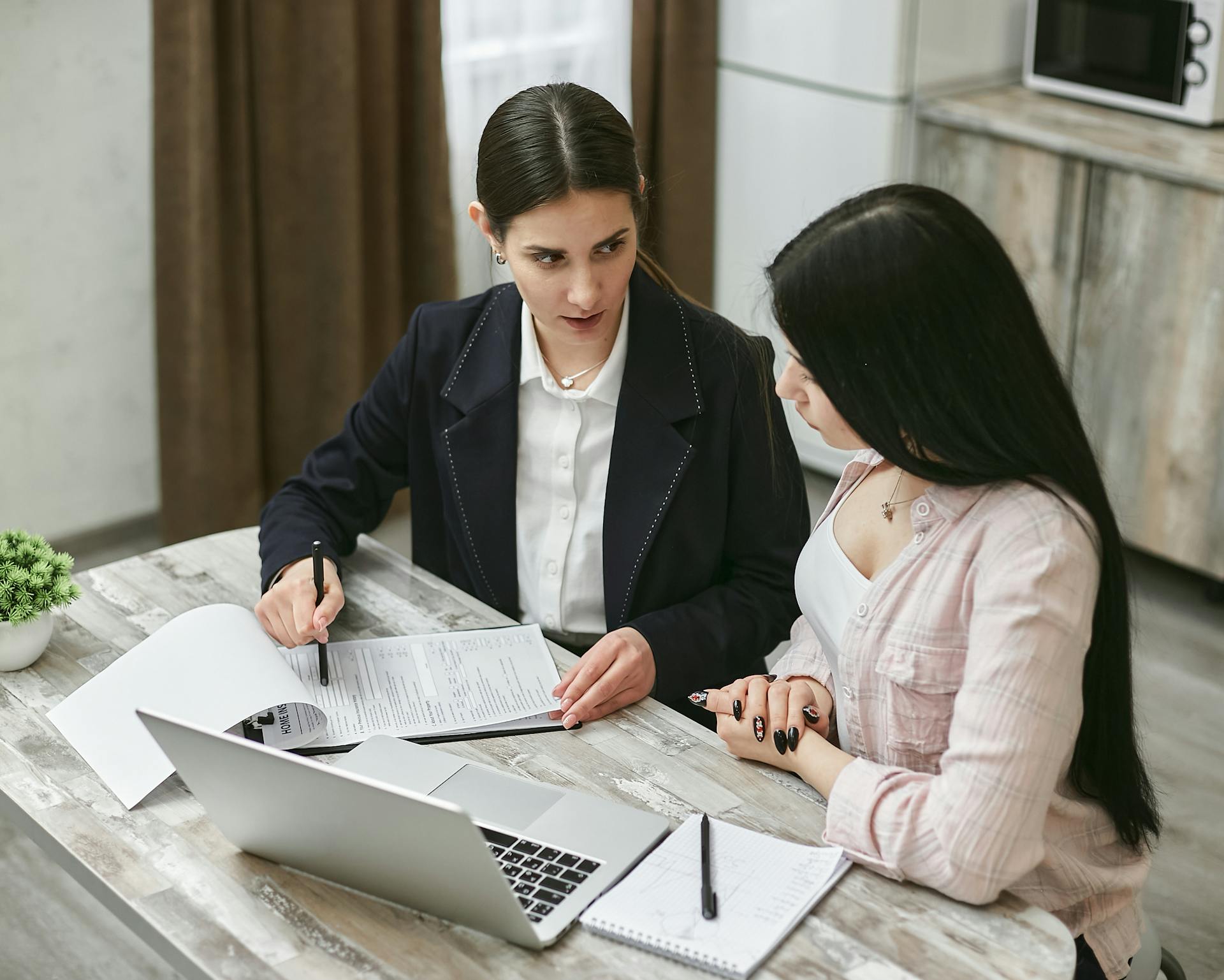 Two businesswomen engaged in a contract discussion at an office table.