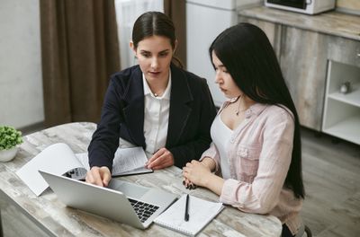 Hai người tại một chiếc bàn gỗ cùng nhìn vào màn hình laptop trong một căn bếp gia đình