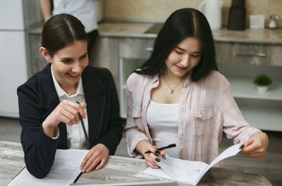Hai người phụ nữ ngồi tại bàn bếp cùng nhau xem qua giấy tờ