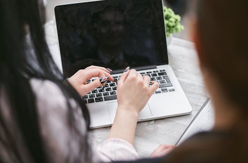 Selective Focus Photo of a Woman with Black Nail Polish Typing on a Laptop