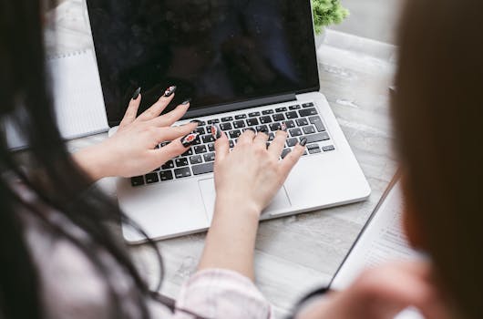 Close-up of a woman's hands with manicured nails typing on a laptop, highlighting professional work environment.