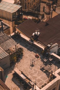 Rustic rooftop garden terrace in urban setting with potted plants and furniture seen from above.