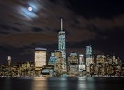 在满月与反光水域的映衬下，纽约市的天际线呈现出迷人的夜景