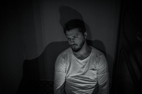 Free A thoughtful man in a dimly lit room, captured in a grayscale portrait with moody shadows. Stock Photo