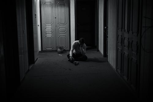 A Grayscale of a Lonely Man Sitting on the Floor