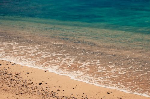 Free Idyllic beach scene with gentle ocean waves meeting the sandy shore under a clear sky. Stock Photo