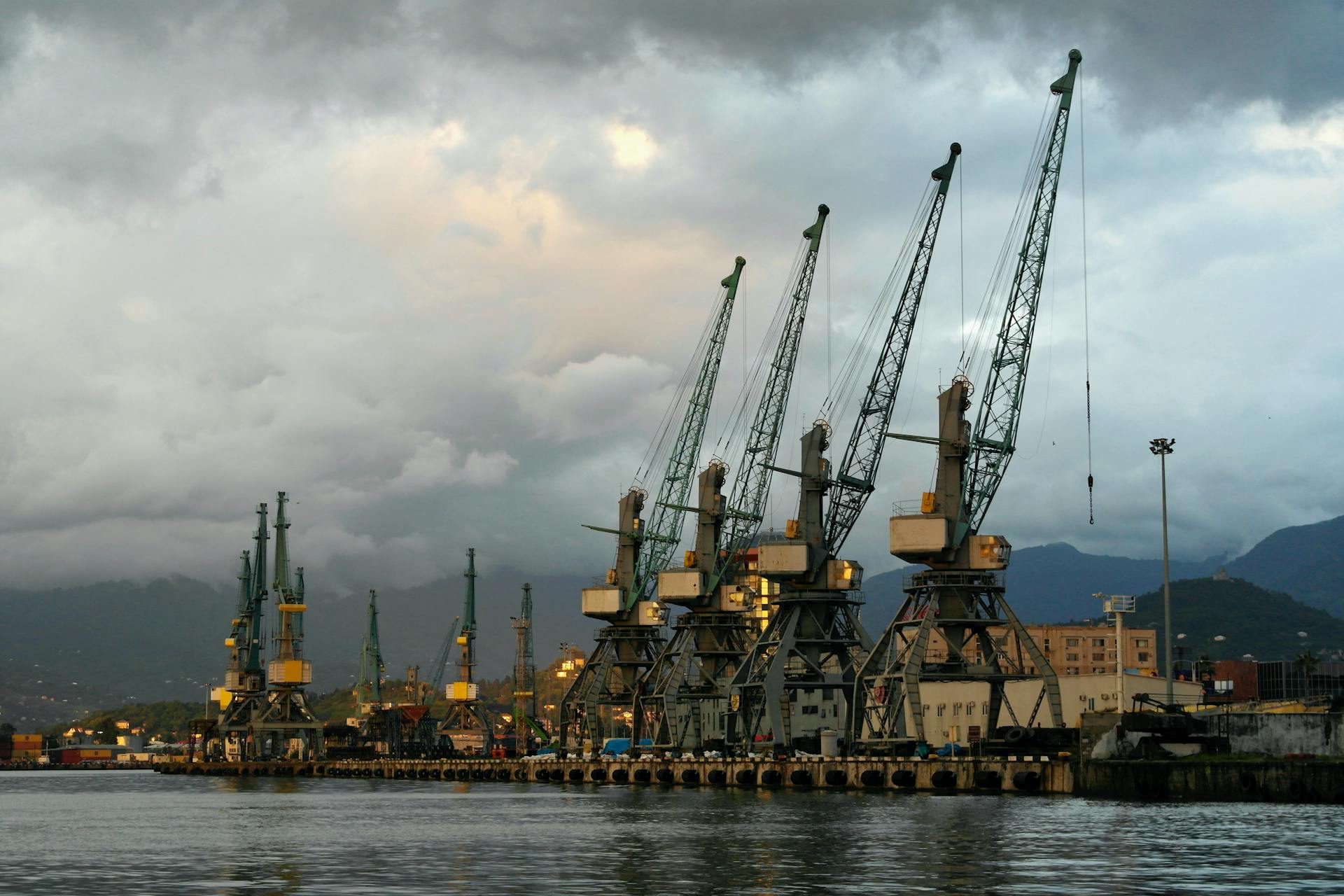 Seaport with industrial cranes against a cloudy sky during twilight, capturing a serene industrial landscape.