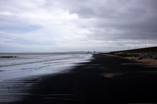 Free A gloomy day at a seashore featuring waves, dark sand, and an overcast sky. Stock Photo
