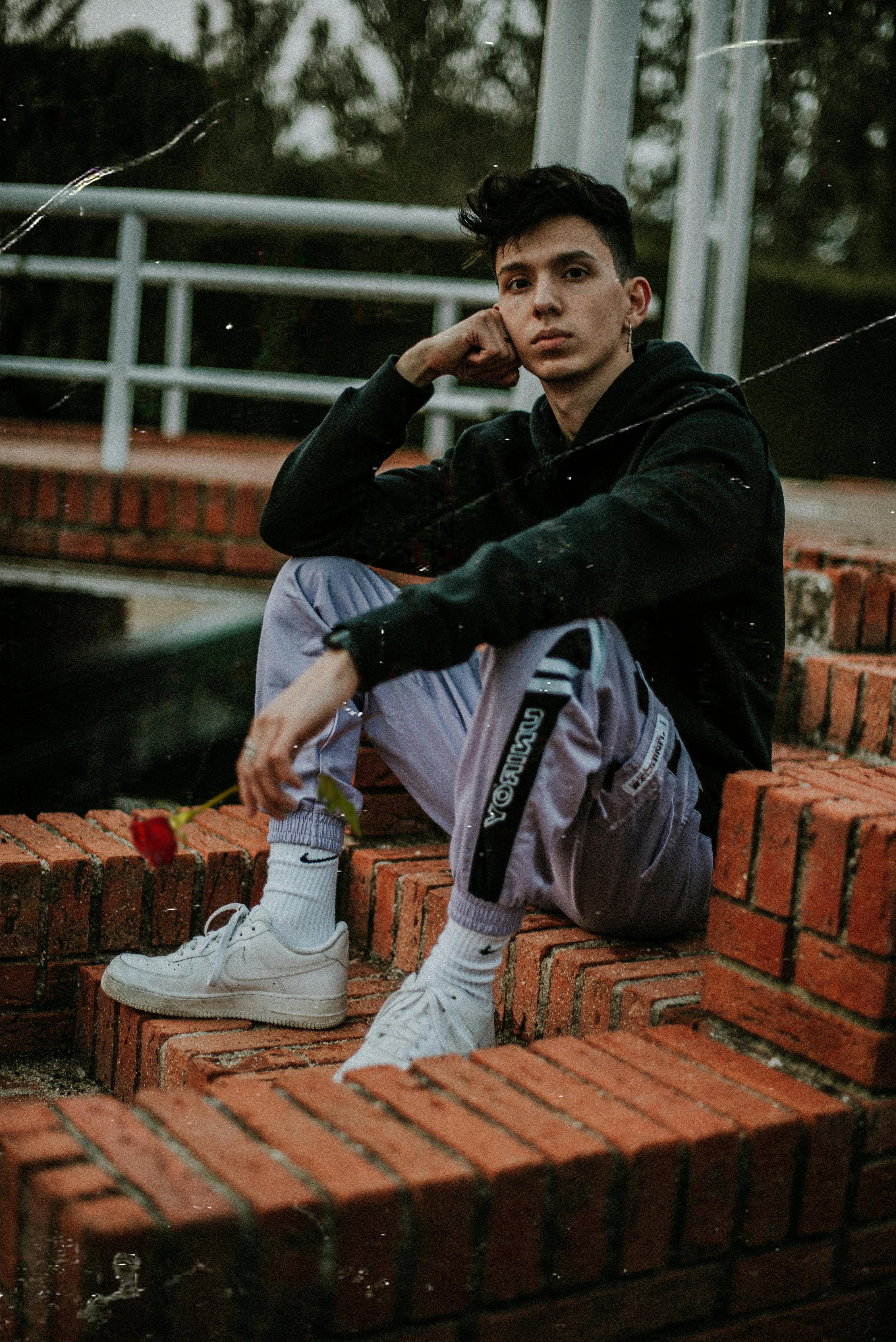 A fashionable young man sits on brick stairs in stylish attire, exuding urban coolness.