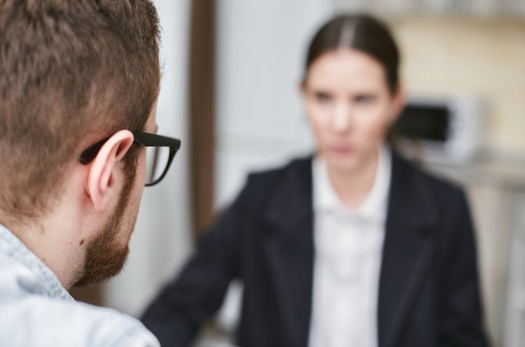 A Man Wearing Black Framed Eyeglasses In Front Of A Woman In Black Blazer