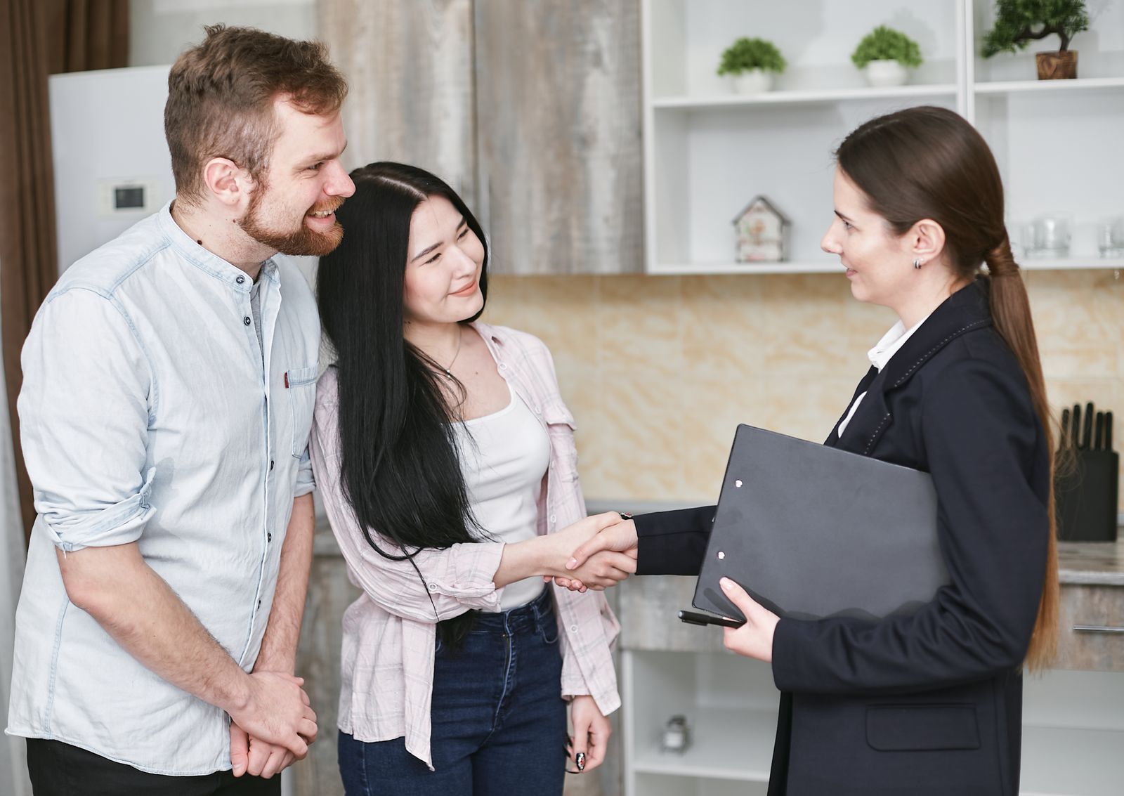 Free A real estate agent greets a couple with a handshake in a modern home interior. Stock Photo