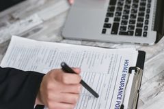 An adult reviews and signs a home insurance policy document on a clipboard next to a laptop.