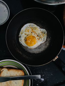 Close-up of a sunny side up egg cooking in a frying pan with toast nearby.
