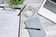 Flat lay of a workspace with a home insurance policy, laptop, and notebook on a desk.