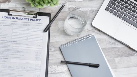 Flat lay of a workspace with a home insurance policy, laptop, and notebook on a desk.
