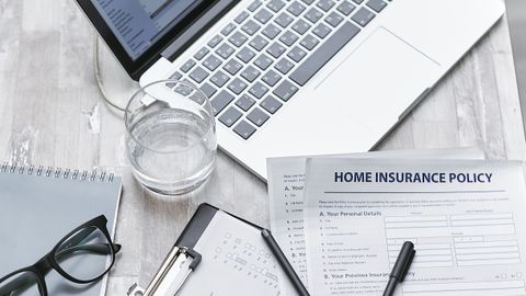 Top view of a desk with laptop, insurance forms, and office supplies, ideal for business or finance topics.