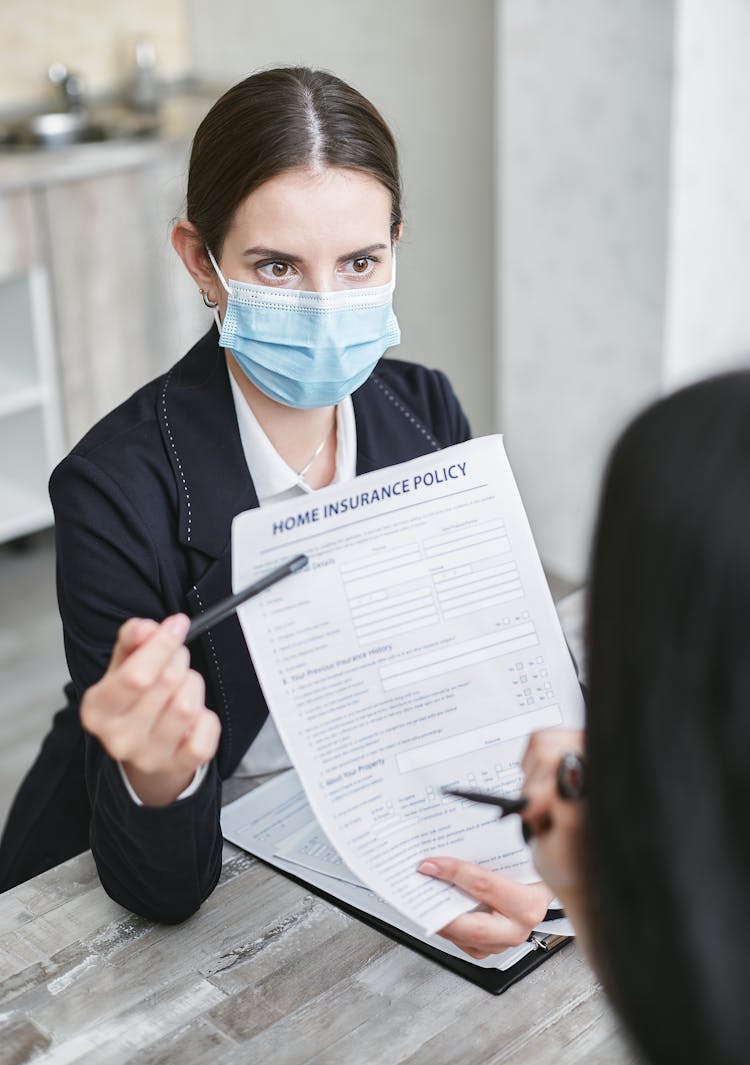 A Woman Wearing Face Mask Holding A Home Insurance Policy