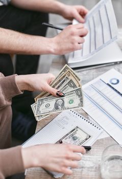 Two individuals counting dollar bills and reviewing financial documents indoors.