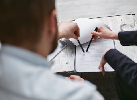 Two individuals analyzing a business contract with pens on a wooden surface.