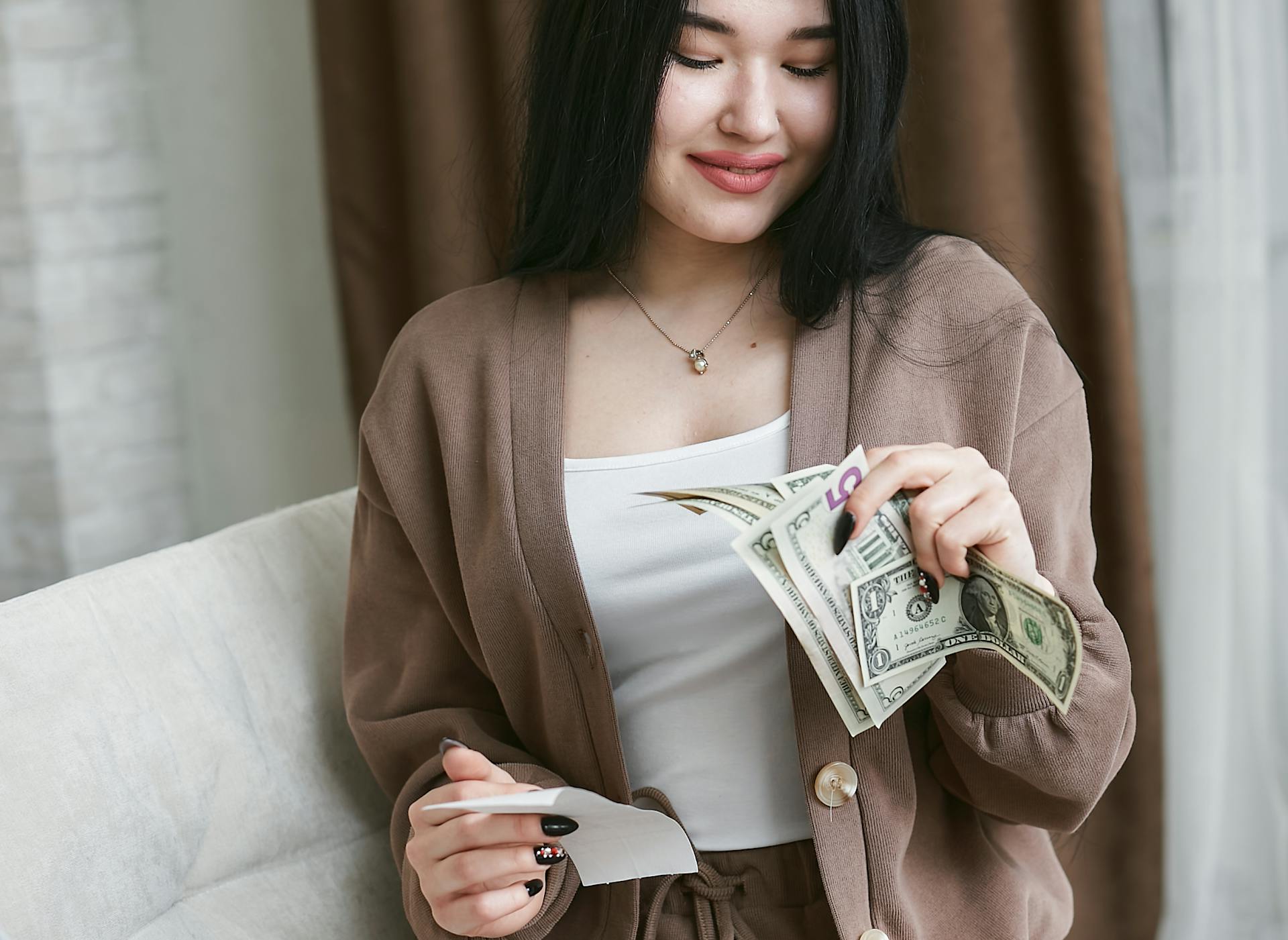 Asian woman happily counting US dollars, symbolizing financial planning and success.