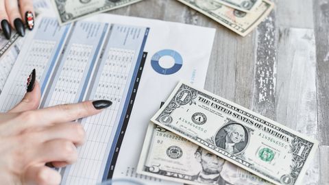 Close-up of hands analyzing financial document with US dollar bills on table.