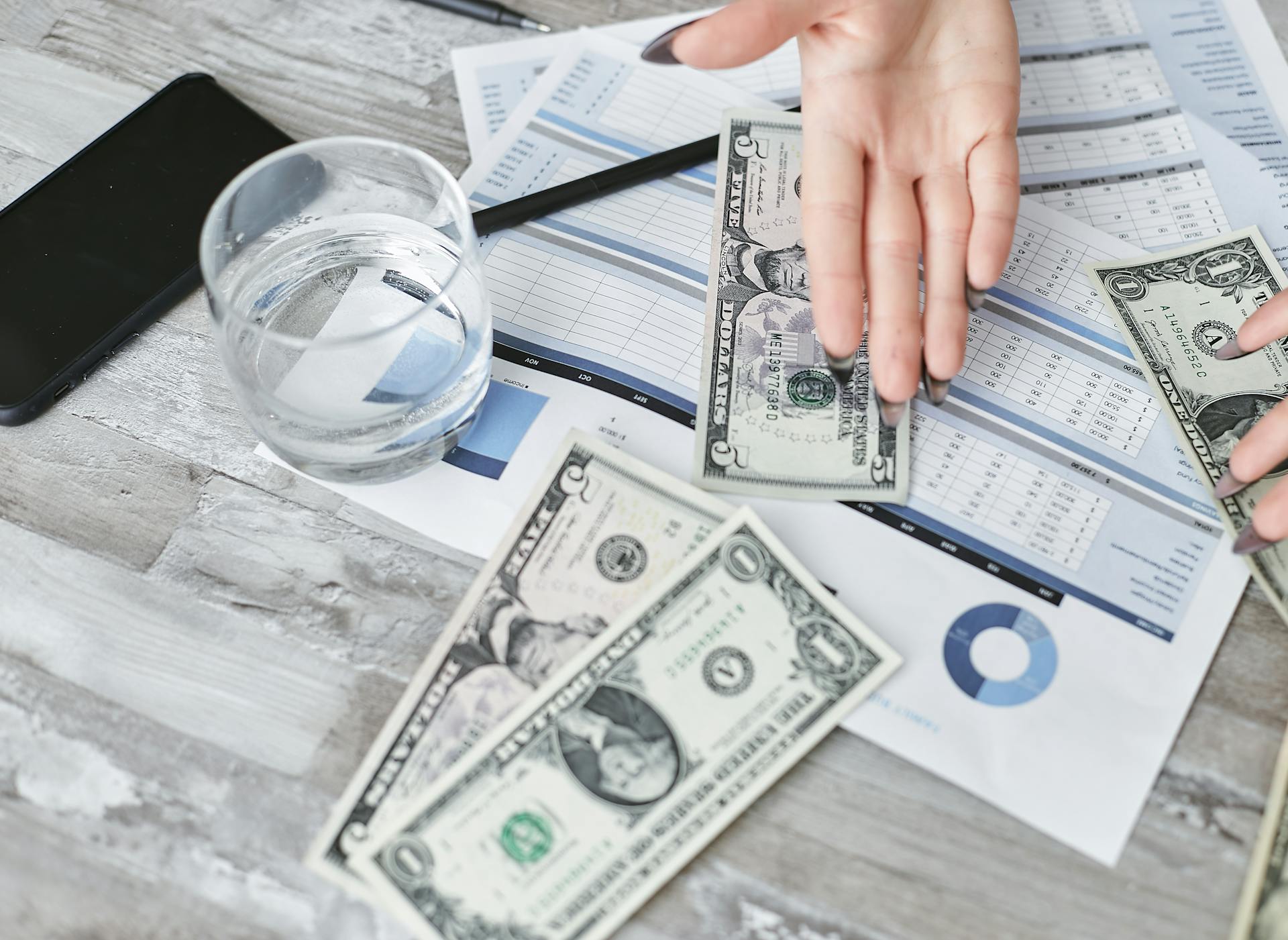 A top view of financial documents with dollar bills and a glass of water, emphasizing budgeting.