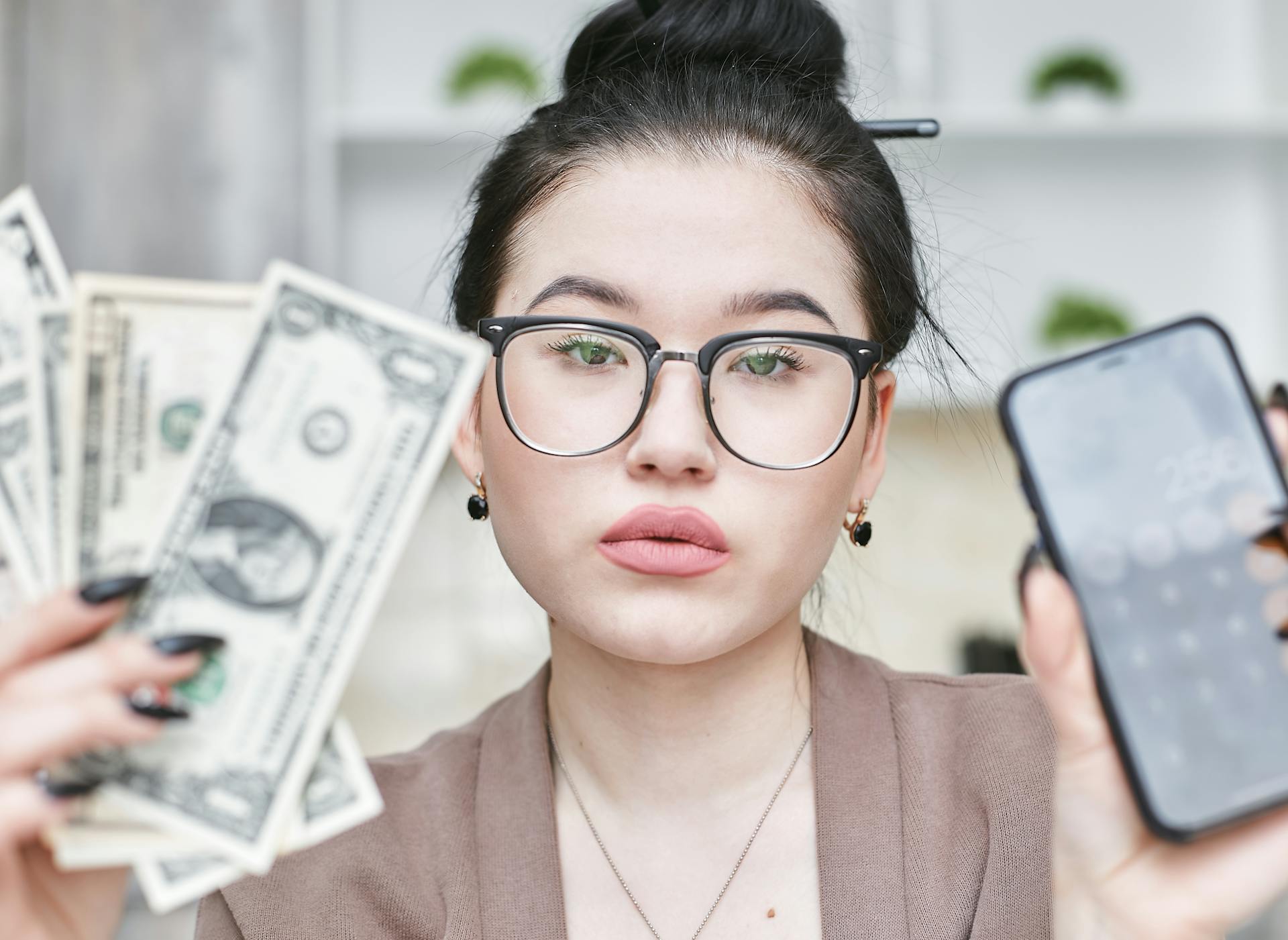 A Woman Holding an iPhone and Cash Money