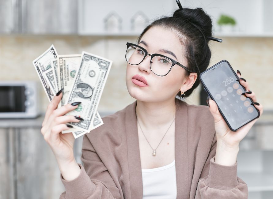 Woman using money-saving apps on smartphone while holding cash — best apps to save money in 2026